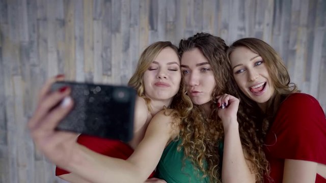 Close-up of three charming girls taking fun selfie on smartphone indoor.