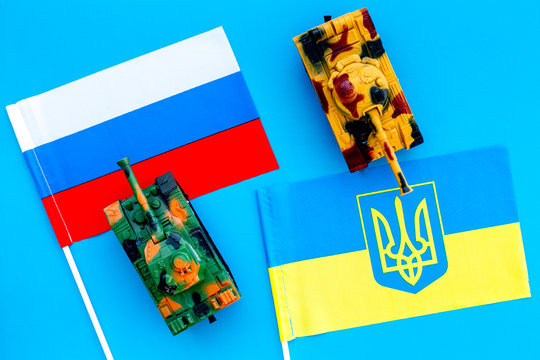 War, confrontation concept. Russia, Ukraine. Tanks toy near russian and Ukrainianflag on blue background top view