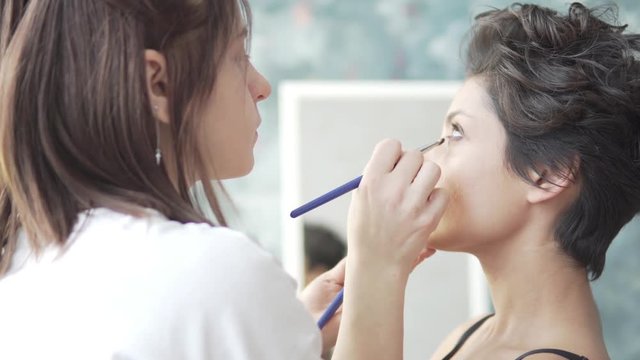 Preparing the model for shooting. Makeup artist paints a beautiful young girl with short dark hair. She does eye makeup. Close-up. Side view. eye makeup