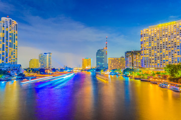 Fototapeta na wymiar Beautiful night view during twilight with cruises and modern business buildings along the Chao Phraya river under blue sky background at Taksin Bridge, Bangkok, Thailand.