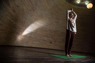 Meditating woman standing on the yoga mat with hands over her head