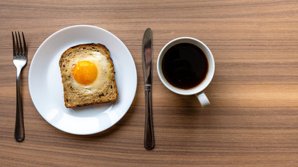 Breakfast concept. White plate with baked bread and egg and white coffee cup. Wooden texture background.