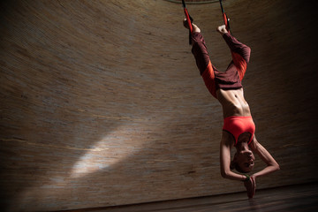 Woman practicing aerial yoga with her legs in the straps