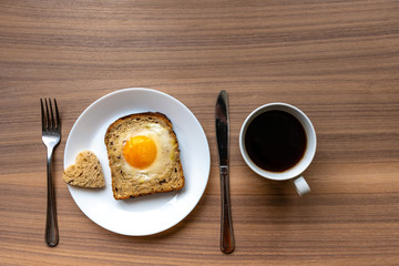 Breakfast concept. White plate with hearts of bread, baked bread and egg and white coffee cup. Wooden texture background.