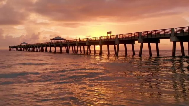 Sunrise dolly view through pilings of Pier at Juno Beach Florida