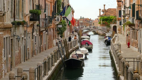 Narrow Canal In Venice Italy With Boats Tied Up As Tourists