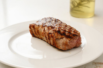 roasted veal fillet, young beef meat on a white plate, rosemary oil in the background, copy space