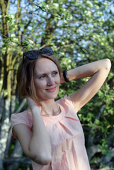 Naklejka premium Young beautiful girl stays near an apple tree with wreath made of flowers of apple tree