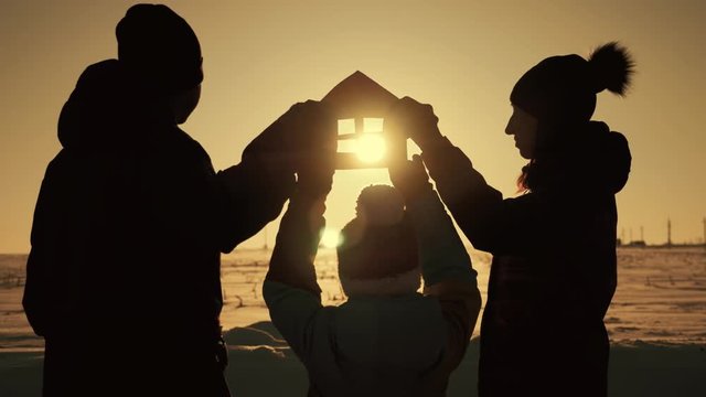 The family holds a paper house at sunset, dreaming of their own home. Silhouette of a paper house in hands at sunset in the sun.