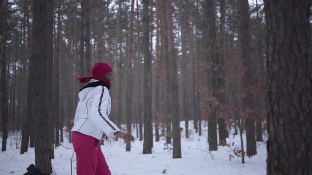 Scared African american pretty woman dressed warm wearing a red hat, scarf and white jacket running through the snowy forest. The girl constantly looks back running away from the pursuer. Slow motion.