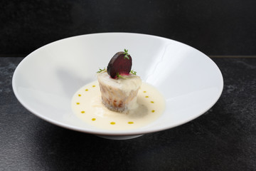 pike fish roll with beetroot and cress garnish in a creamy sauce in a deep bowl on a dark slate background, copy space
