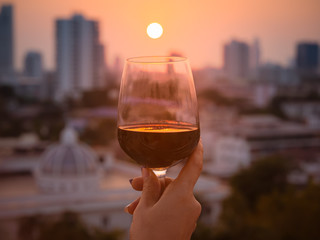 Happy moment of woman hand with red wine into glasses in a sunset background as on the rooftop at the bar restaurant