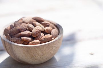 Almond nut in wooden bowl on wood table with green leaf background, copy space