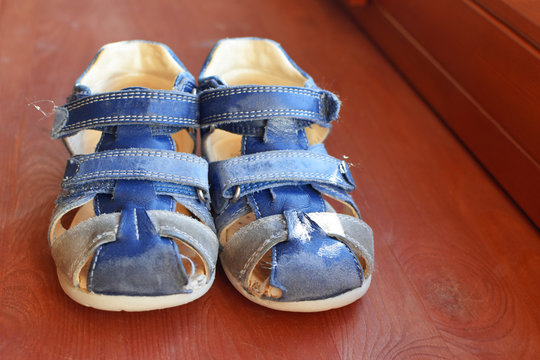 Old Worn Out Blue Leather Baby Boy Sandals Shoes On Brown Wooden Background.