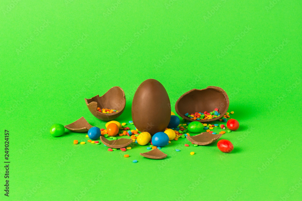 Wall mural Easter chocolate egg and multi-colored sweets and broken chocolate eggs on a green background. Easter celebration concept