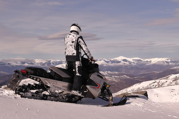 RIDER WITH A SNOWMOBILE AT THE SUMMIT OF A SNOWED MOUNTAIN IN WINTER WITH MOUNTAINS IN THE HORIZON