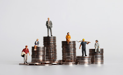 Coin piles and miniature people. The concept of the gap between the rich and the poor in society.