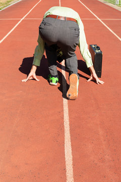 A businessman in gray suit with green shirt, black briefcase and broken green sports shoes getting ready on a running track