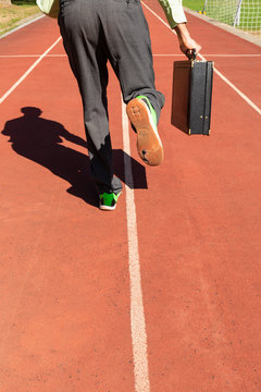 A business man in gray suit with green shirt, black briefcase and broken green sports shoes running on a running track