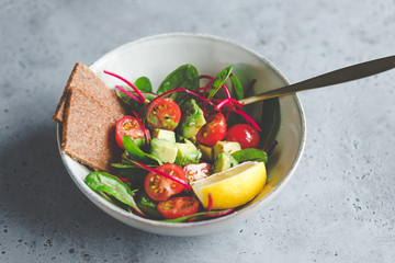 Vegetarian healthy salad is made from swiss chard leaves, cherry tomatoes, avocado, lemon juice and olive oil into a ceramic portion bowl.