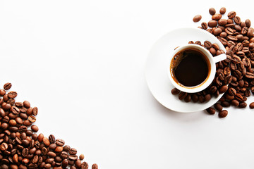 Coffee cup with roasted brown beans scattered on white table with a lot copy space for text. Flat lay composition. Close up, top view, background.