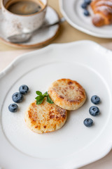 Cheesecake, fresh blueberry and cappuccino. Cottage cheese pancakes or curd fritters on white plate. Healthy and diet breakfast at sunrise