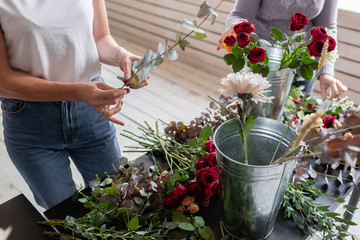 Close-up flowers in hand. Florist workplace. Woman arranging a bouquet with roses, chrysanthemum,...