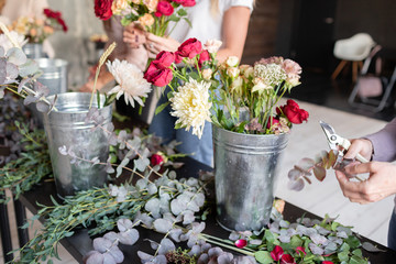 Close-up flowers in a metal bucket. Florist workplace. Woman arranging a bouquet with roses,...