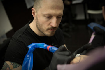 A tattoo artist with gloves paints a tattoo