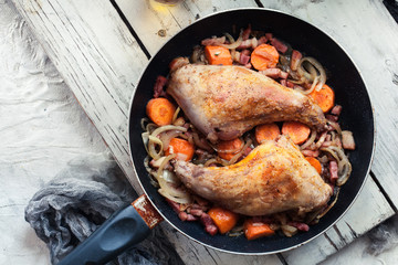 Fried rabbit legs on frying pan with vegetables