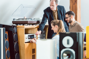 Couple testing a Hi-Fi system in the store with the salesman explaining