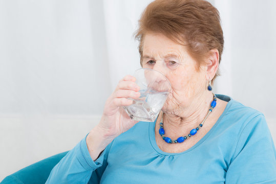 Seniorin trinkt ein Glas Wasser gegen ihre Kopfschmerzen