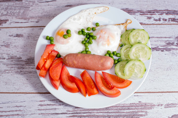 Homemade fried eggs with sausages on a white plate, on a wooden background. Classic breakfast. View from above.