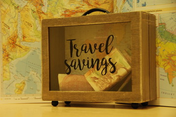 Money savings for traveling in suitcase shaped money-box on world map background 