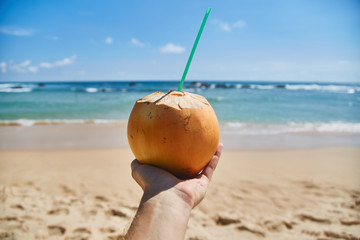 a man holds a coconut with a straw on the ocean. Guy drinks juice from a coconut on the ocean