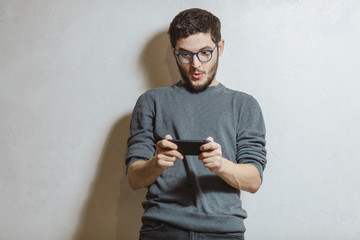 Portrait of young man playing video games on smartphone, over white textured background.