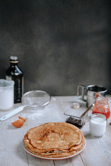 Breakfast with russian bliny or thin sweet crepes, jam and yogurt on a rustic wooden table in daylight