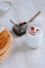 Breakfast with russian bliny or thin sweet crepes, jam, berries and yogurt on a rustic wooden table in daylight