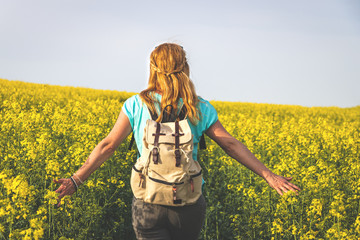 Naklejka na ściany i meble Happy woman with backpack walking in blooming oilseed field at spring