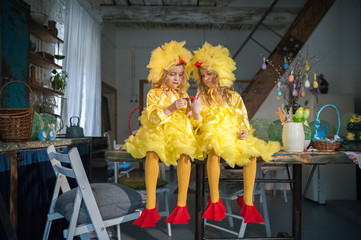 Twin sisters at Easter eat ginger cookies, painted eggs, laugh. Girls in the kitchen in costumes chicken.
