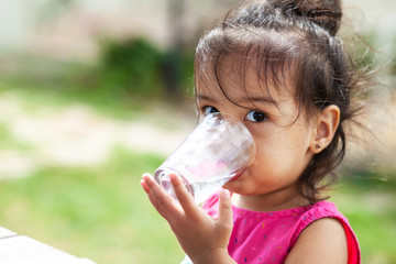 Cute child girl drinking clear water outdoors. Pure water