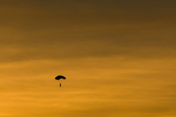 Silhouette of parachutist flying slowly on parachute in the beautiful sky at sunset.