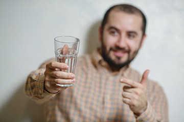 Portrait of young man holding a glass of water and pointing with his finger.