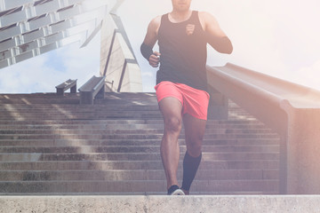 Fototapeta na wymiar Muscular hispanic Young male dark-skinned athlete running up a flight of stairs with speed, sporty young man in black t-shirt training or working out outdoors while jogging up the steps. Flares