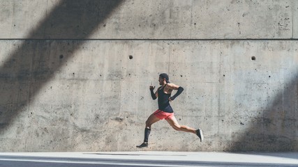 Muscular Male athlete sprinter running fast,exercising outdoors,jogging outside against gray concret background with copy space area for text message or advertising content.Side view,full length.Wide