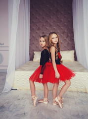 Two little girls in red tutu posing in a room.
