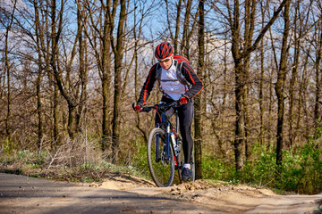 Sports cyclist rides along a trail in the forest on a spring sunny day.