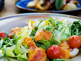 Fresh Shrimps, Mango salad with lettuce green mix, cherry tomatoes, herbs and olive oil, lemon mango dressing. healthy food on wooden table with blurry background in the restaurant 