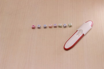 pregnancy test pack positive result at wooden Table and text positive from colorful alphabet cube bead