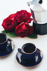 Two coffee mugs and a coffee pot on a table decorated with roses